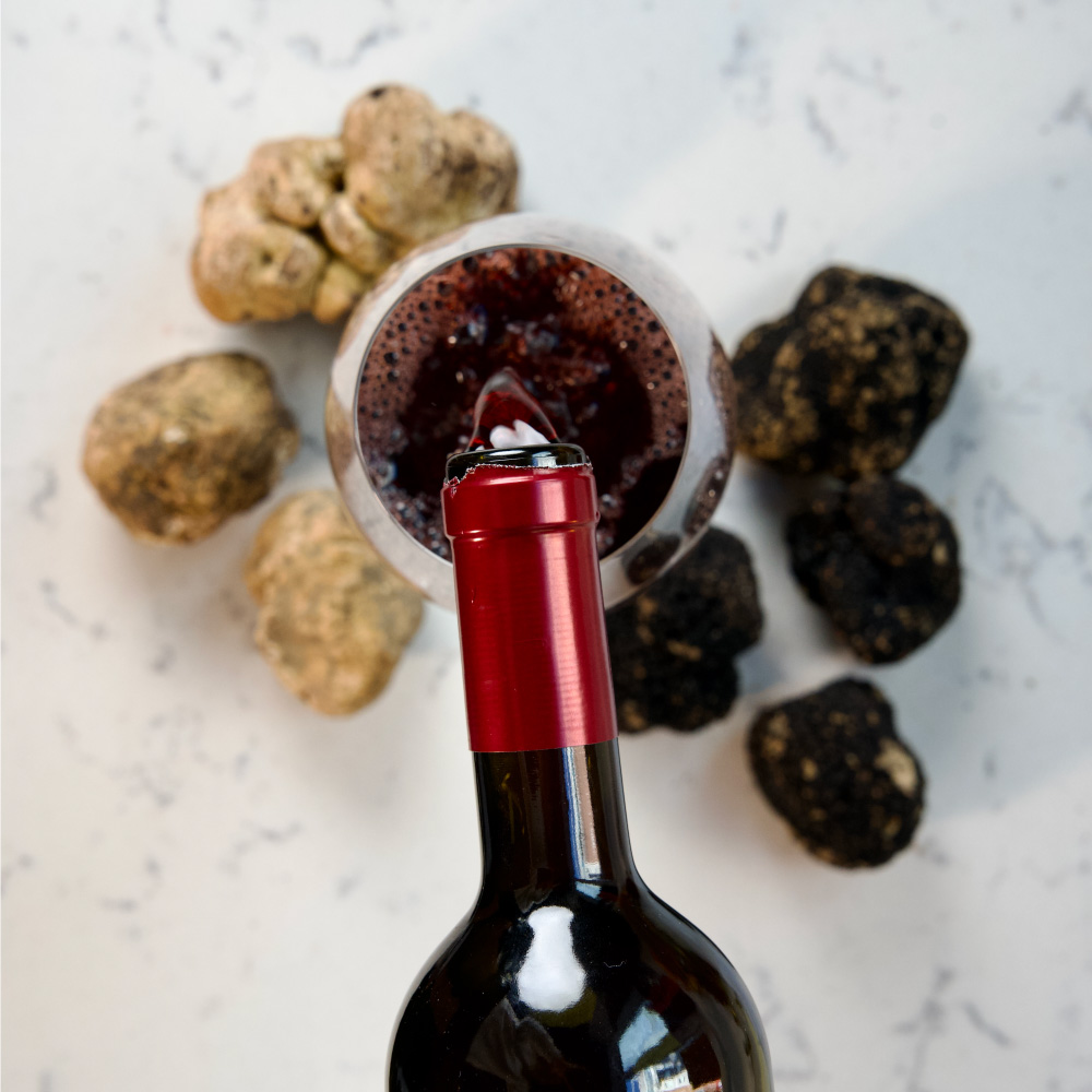 Bottle of fine Italian red wine being poured. Truffles and marble counter in the background